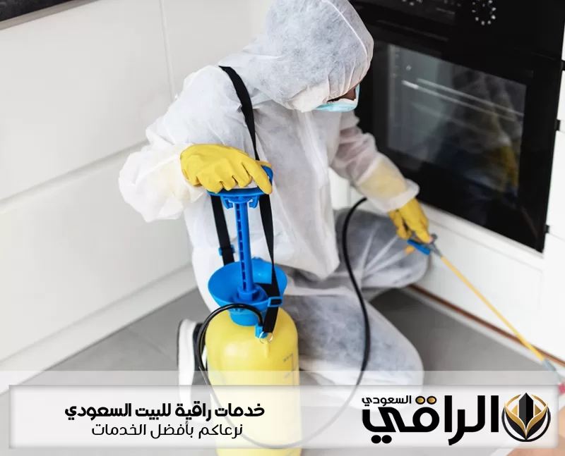 فني شركة مكافحة الحشرات بتيماء يرتدي بدلة واقية ويرش المبيد حول فرن المطبخ باستخدام مضخة متخصصة بدقة